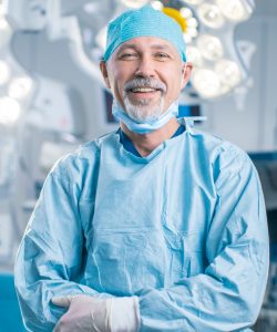 Portrait of the Professional Surgeon Looking Into Camera and Smiling after Successful Operation. In the Background Modern Hospital Operating Room.